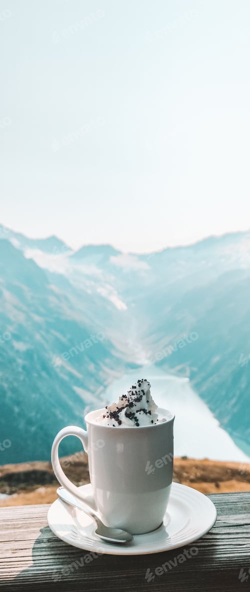 Preview: Vertical shot of a cup of coffee with cream on a window with the rocky mountains in the background