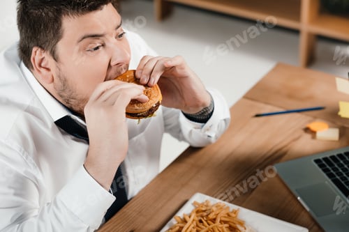 Preview: overweight businessman eating hamburger at workplace