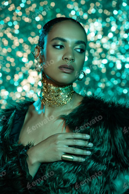 Preview: stylish african american woman in faux fur jacket and gold on neck posing on shiny blue background