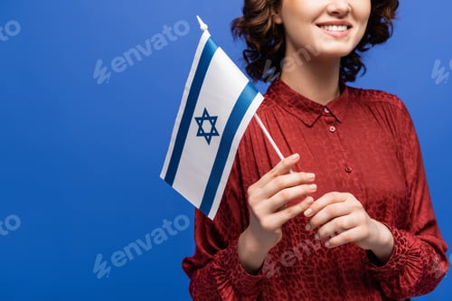 Preview: cropped view of smiling Hebrew teacher holding flag of Israel isolated on blue