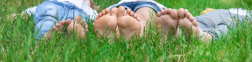 Preview: Children's feet on the green grass in the park. Selective focus.
