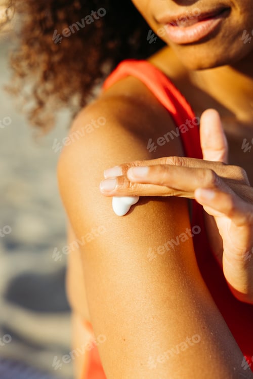 Preview: Young woman applying sunscreen on her shoulder at the beach