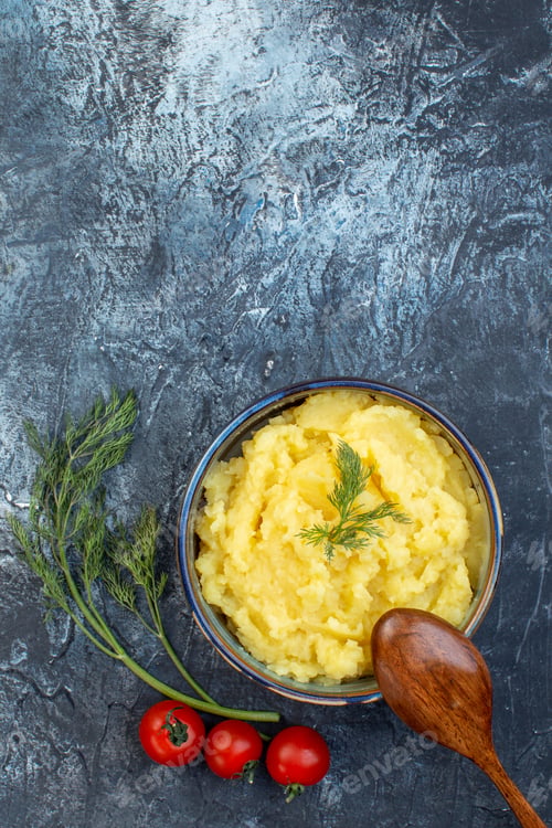 Preview: Overhead view of mashed potatoes served with dill wooden spoon fresh tomatoes on dark color