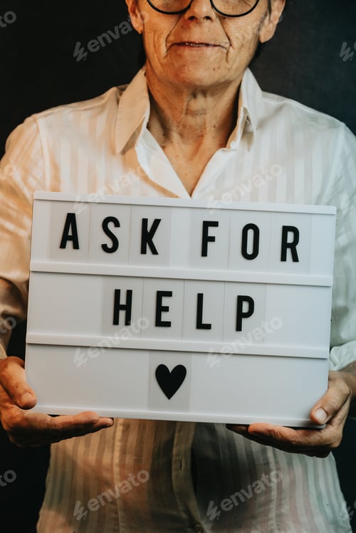 Preview: Close up of an old woman holding a sign that says ask for help, while smiling to camera