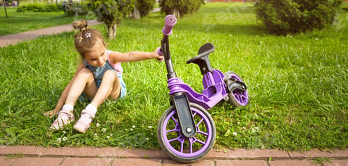 Preview: Cheerful girl sitting resting on the grass in a park near to the purple running bike