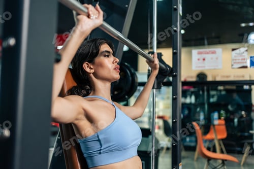Preview: Caucasian young sportswoman lift up weight machine or barbell in gym.