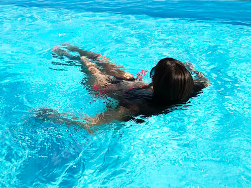 Preview: Young Woman With Long Hair Wearing Sunglasses Swimming in Swimming Pool With Blue Clear Water