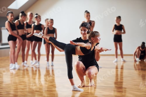 Preview: Woman teaching and helping. Group of female kids practicing athletic exercises together indoors