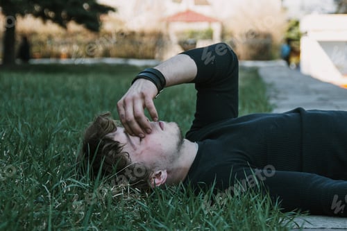 Preview: upset guy lies on the lawn and covers his face with his hand