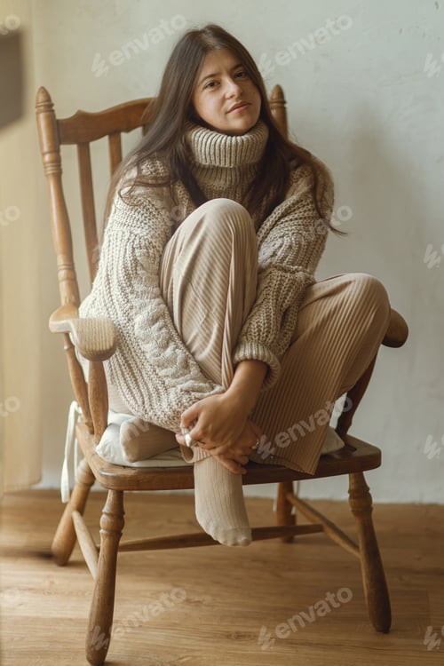 Preview: Stylish woman in cozy knitted sweater sitting in vintage wooden chair posing