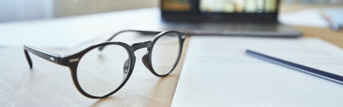 Preview: Close up of eyeglasses on the table. Laptop screen with female teacher communicating via video