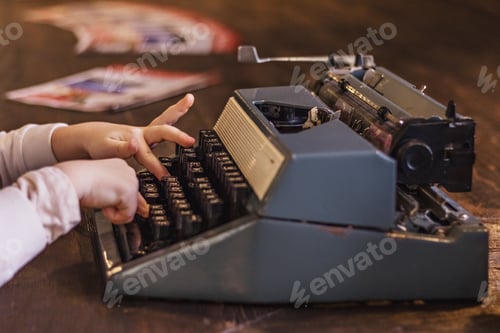 Preview: Vintage old typewriter on a wooden table and child's hands on the keys. Some keys are broken.