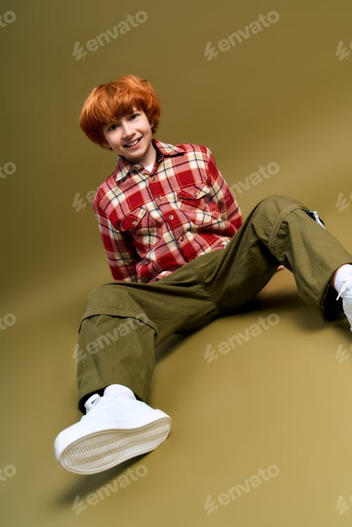 Preview: Stylish little boy in trendy outfit poses playfully against a warm backdrop