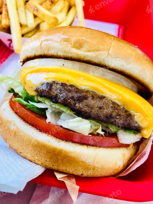 Preview: Closeup of a cheeseburger with lettuce, tomato, and a side of fries.