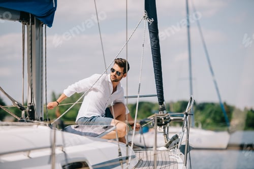 Preview: handsome young man in sunglasses looking away while sitting on yacht