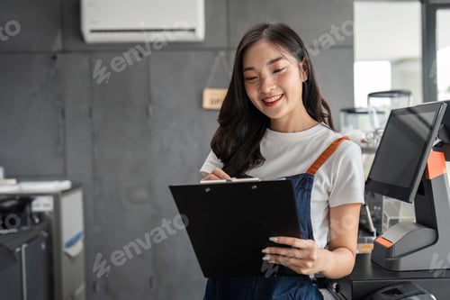 Preview: Young Barista Managing a Modern Coffee Shop with a Smile, Holding a Clipboard and Wearing an Apron