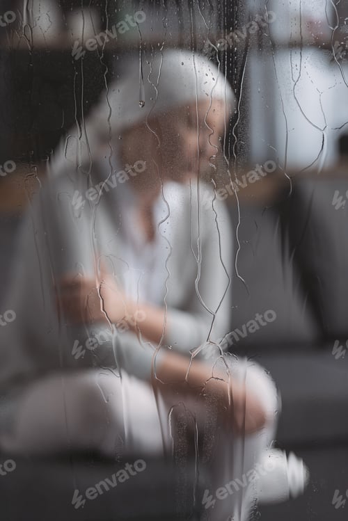 Preview: close-up view of glass with raindrops and sick mature woman behind