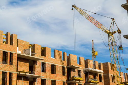 Preview: Construction site of a new apartment high building with tower cranes against blue sky.