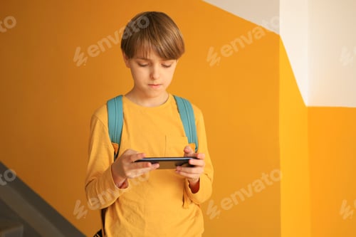Preview: A handsome teen boy in a yellow T-shirt stands with a phone near a yellow wall. Using technologies