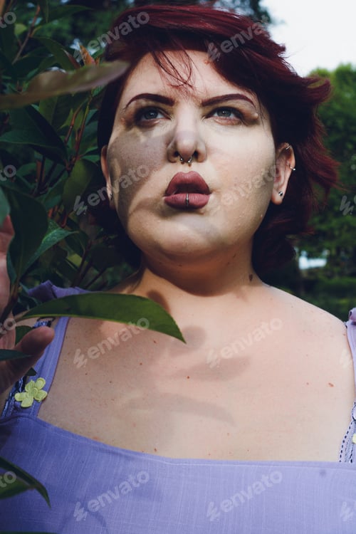 Preview: Vertical portrait of a young plus-size Argentinian woman in a park next to a bush
