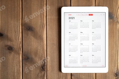 Preview: a tablet with an open calendar for 2021 year on a wooden boards table background. space for text.