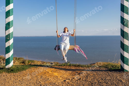 Preview: Attractive girl in casual clothes swinging on an outdoor swing. A happy woman smiles and enjoys life