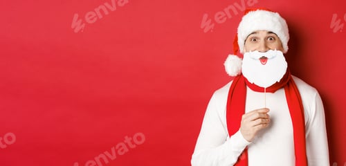 Preview: Concept of christmas, winter holidays and celebration. Portrait of funny man in santa hat, holding