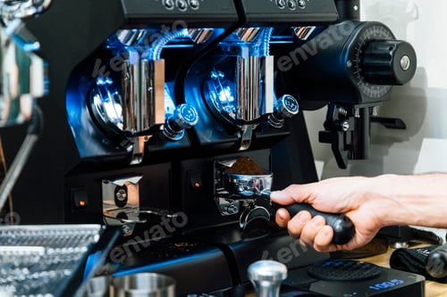 Preview: Close-up view of barista filling portafilter with fresh ground coffee under grinder