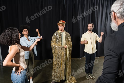 Preview: interracial actors posing near man in king costume near art director on blurred foreground