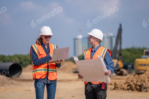 Preview: Construction surveyor or engineer working construction site blueprint and laptop for inspection deta
