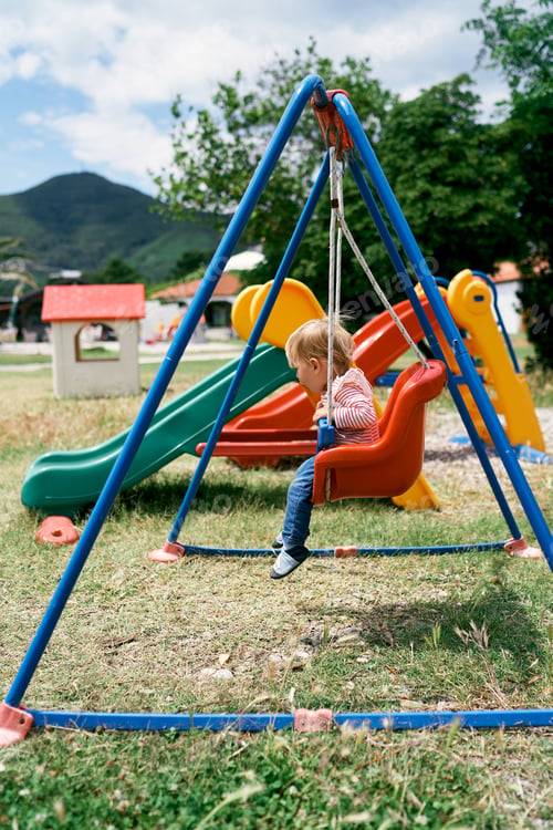 Preview: Small kid sits on a colorful swing. Side view