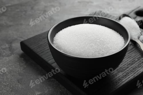 Preview: Granulated sugar in bowl on grey textured table, closeup. Space for text