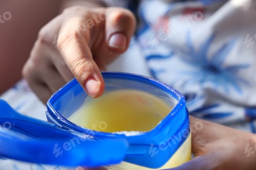 Preview: woman using petroleum jelly onto skin at home close up.