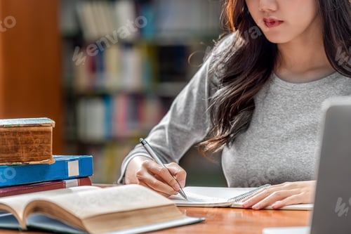 Preview: Closeup Asian young Student hand writing homework and using technology laptop in library
