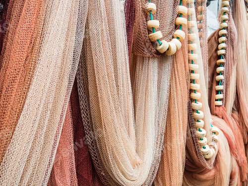 Preview: Closeup shot of hanging multicolored fishing nets and white beads on a green rope