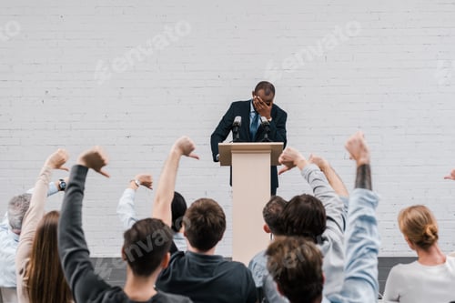 Preview: back view of journalists showing thumbs down near african american speaker covering face