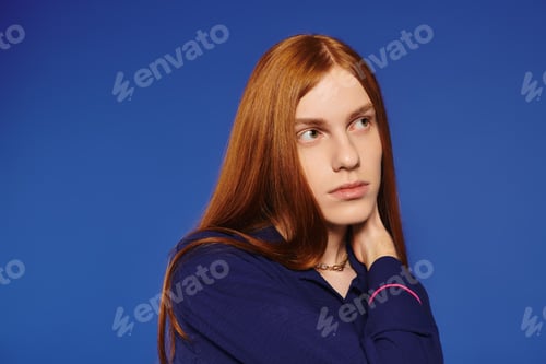 Preview: Stylish young man with long red hair posing against a vibrant blue backdrop