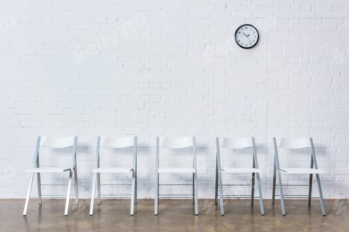 Preview: Row of empty chairs by white brick wall with clock
