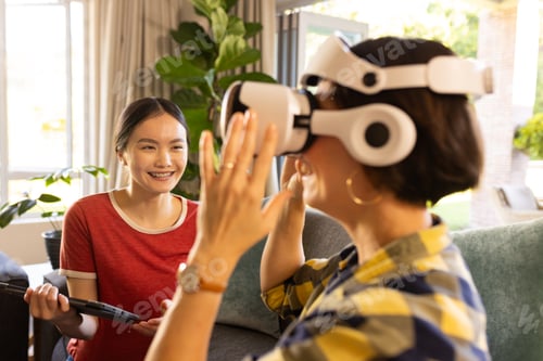 Preview: Using VR headset, mother interacting while girl with tablet smiling nearby