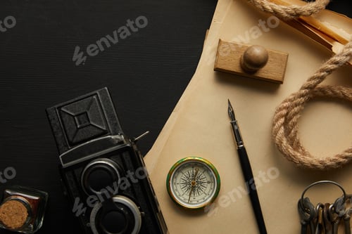 Preview: top view of vintage camera, paper, fountain pen, compass, stamp and keys on black background