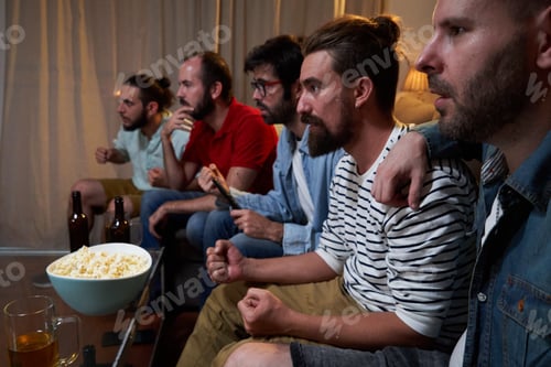 Preview: Group of males concentrated sitting on the sofa in a living room watching a soccer game cup.