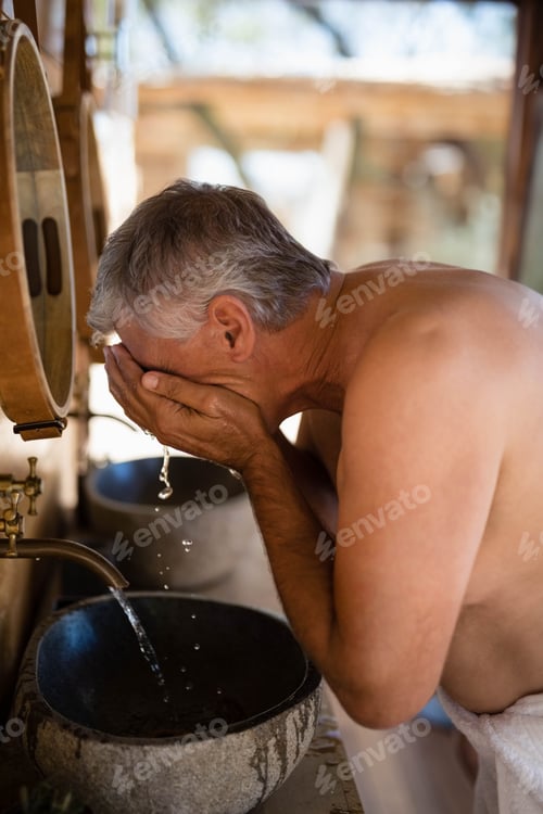 Preview: Senior man washing face over stone basin under brass faucet in open-air pavilion, copy space