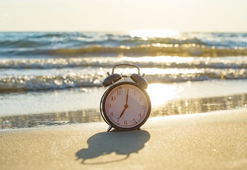 Preview: black retro alarm clock stands on the sand against the background of the sea, 7 am concept of get up