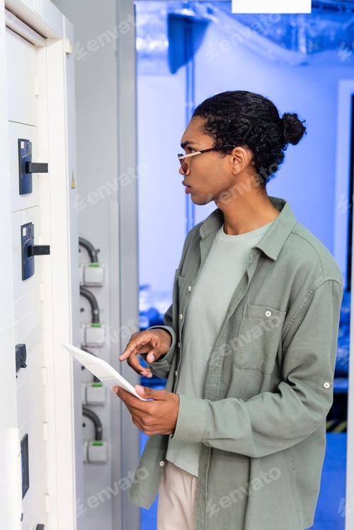Preview: african american engineer pointing at digital tablet while checking switchboard in data center