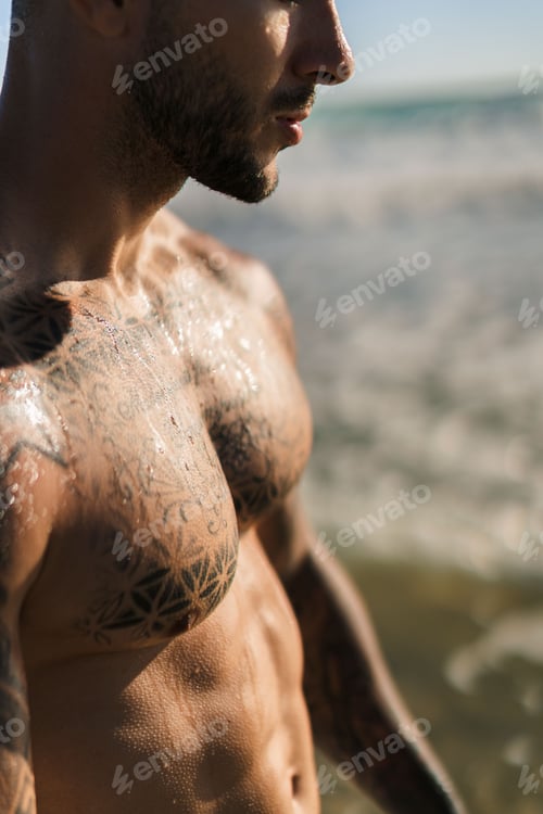 Preview: Vertical partial view of an attractive man at the beach with tattoo on his wet chest