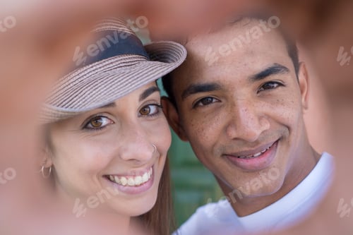 Preview: Closeup portrait of happy young multiethnic couple smiling and doing hearth sigh with hands