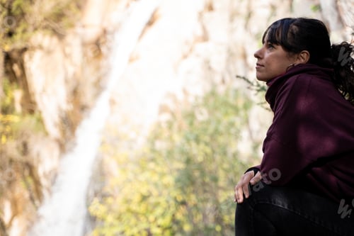 Preview: Profile of a woman sitting while looking at a small waterfall in the forest