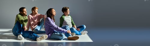 Preview: young men in casual wear sitting on floor looking away on grey backdrop, cultural diversity, banner