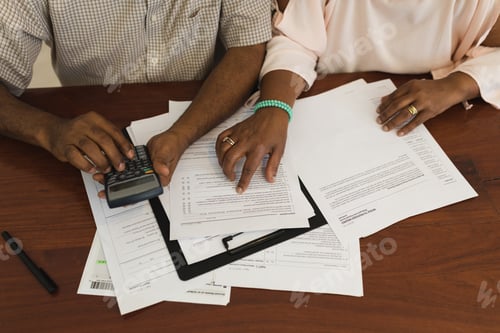 Preview: Mid section of senior African American couple looking at invoices and using a calculator at home