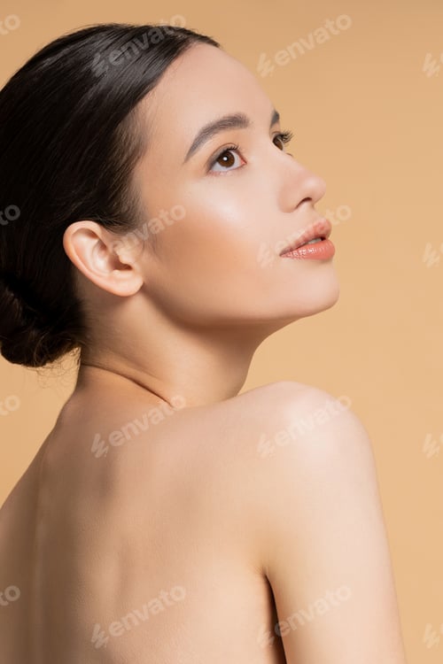 Preview: Pretty brunette woman with naked shoulders looking away isolated on beige